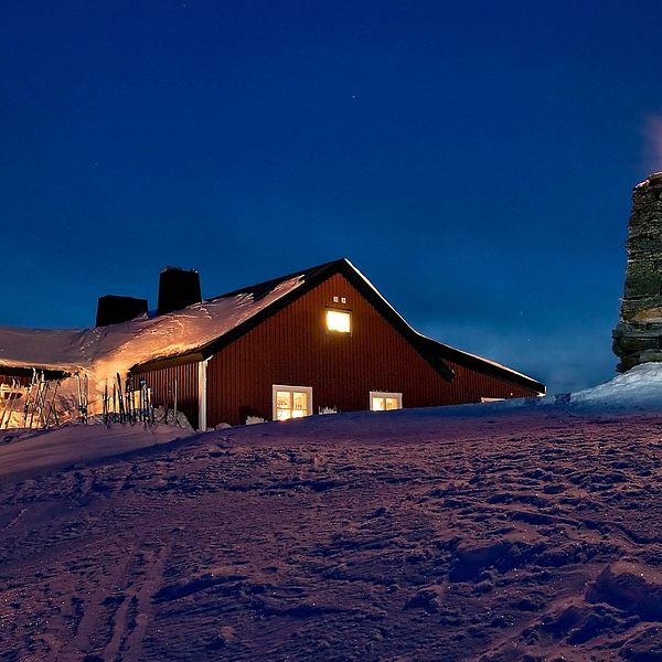 En röd byggnad med en stenfyr till höger. Kvällsljus. Snö och många skidor uppställda framför den röda byggnaden.