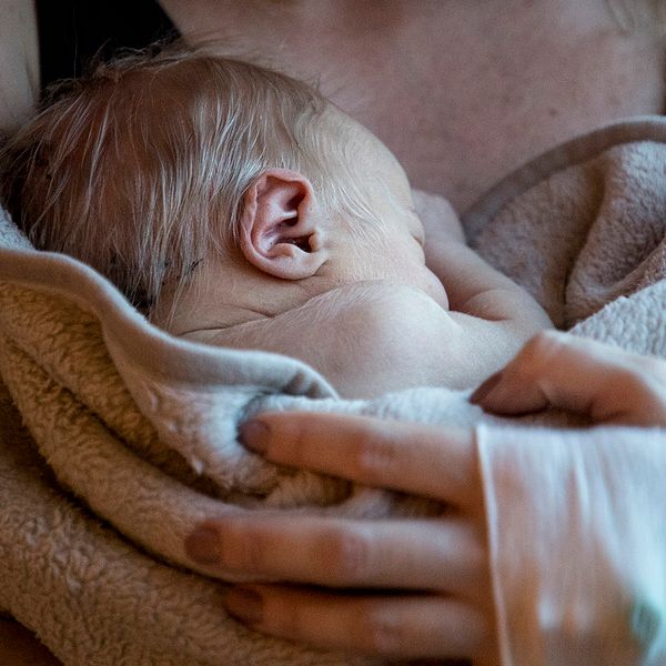 Nyfödd bebis ligger i en kvinnas famn.