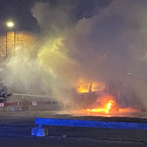 Bild på en brandman som sprutar vatten på en brinnande bil. Det är mycket rök.
