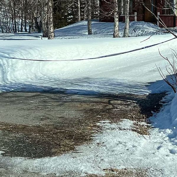 polisband över en uppfart med lite träd och snötäcke, trästuga skymtar