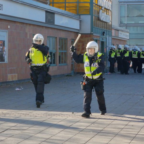 en mängd poliser i hjälm och reflexvästar på en gata i Norrköping, två rör sig mot kameran, en med batongen lyft