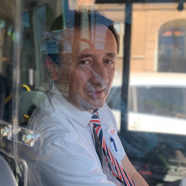 Bild på busschauffören Gjon Hoshi i Eskilstuna. Han sitter i förarsätet på en buss bakom en skiva i plexiglas.
