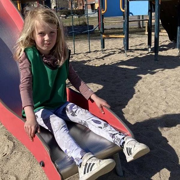 en femårig flicka sitter på botten av en rutschkana i sandtäckt lekpark