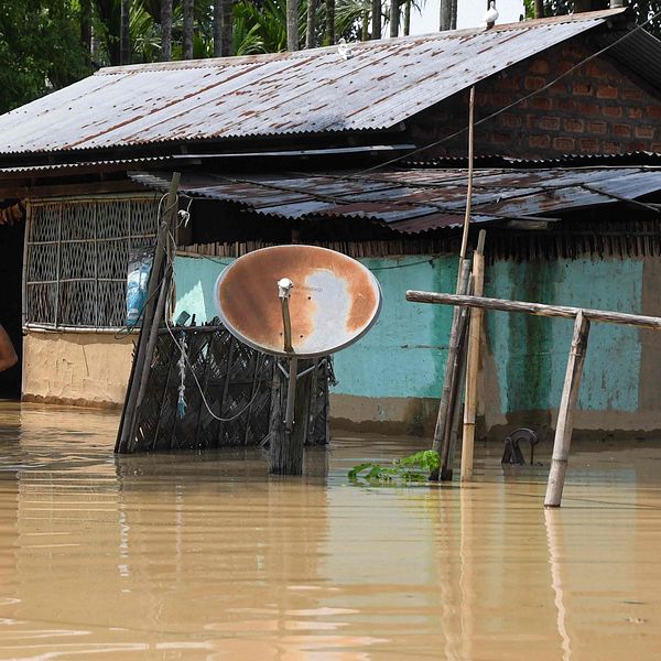 Bilden visar en man som bär sina tillhörigheter genom ett översvämmat område i Indien.