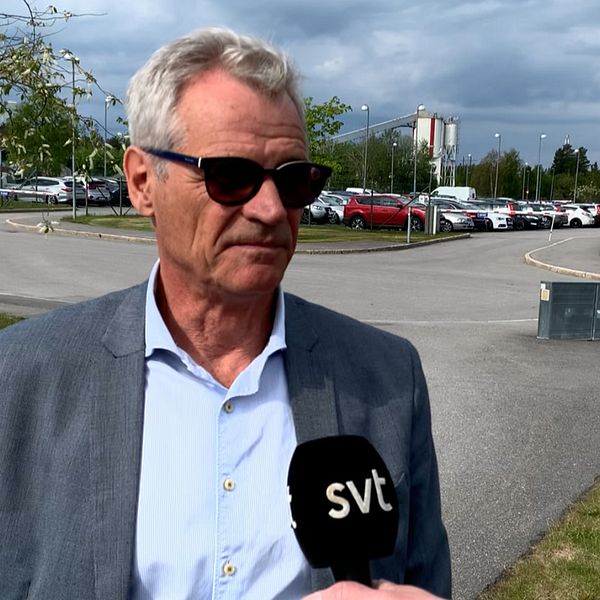 Ulf Holst, i förd skjorta och kavaj och ett par svarta solglasögon, står mitt i bild och en reporter sträcker fram en mikrofon till honom.