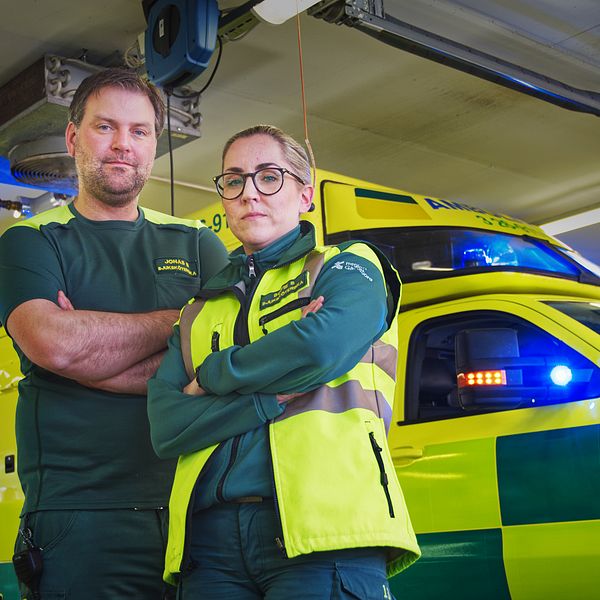 Ambulanssjuksköterskorna Jonas Brindmark och Sofie Smedberg står med armarna i kors framför en ambulans i ambulansgaraget.