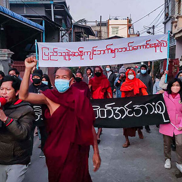 Ungdomsaktivister och buddhistiska munkar deltar i ett protestmöte mot den militära regeringen samtidigt som de håller i en banderoll som lyder på burmesiska: ”Vem vågar stanna på motsatt sida av folkets vilja”, tisdagen den 1 februari 2022, i Mandalay, Myanmar.