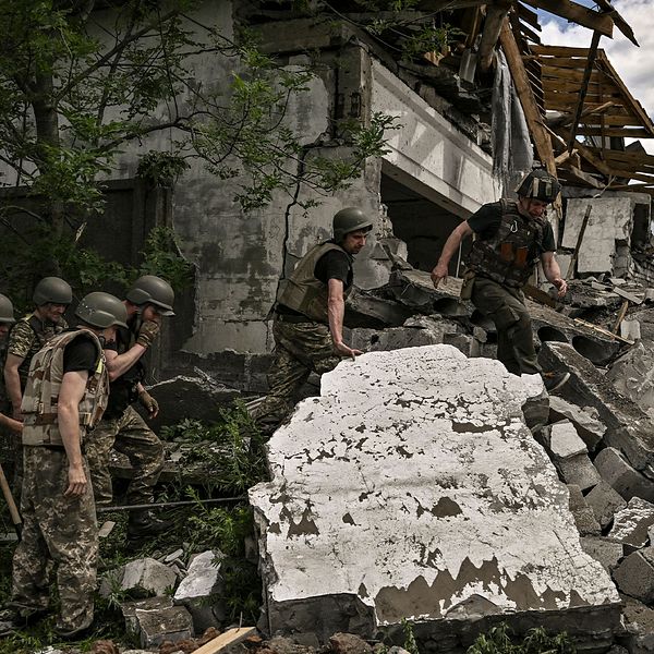 Ukrainska soldater står vid en bombad byggnad.