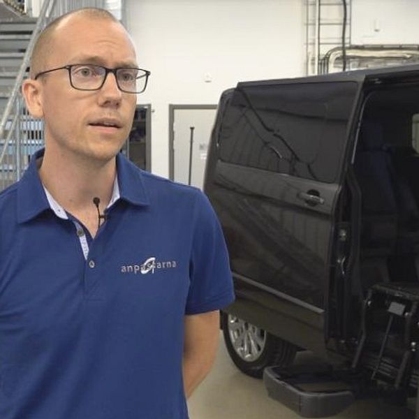 en man intervjuas i en verkstadslokal, bredvid en minibuss.