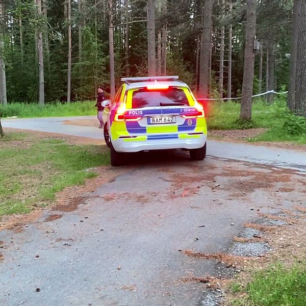 polisbil på cykelväg i skogsområde, tejp-avspärrningar och polismän skymtar längre bort