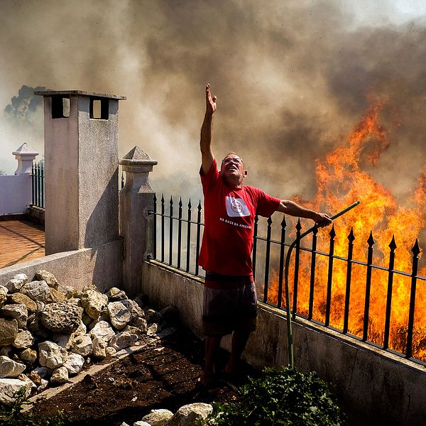 En invånare häller vatten på lågorna under en skogsbrand i Caneças i utkanten av Lissabon, Portugal under söndagen.