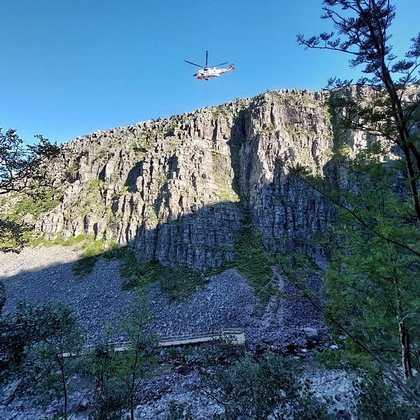 En helikopter vinschar ner en person för att rädda folk som sitter på en bergkant.