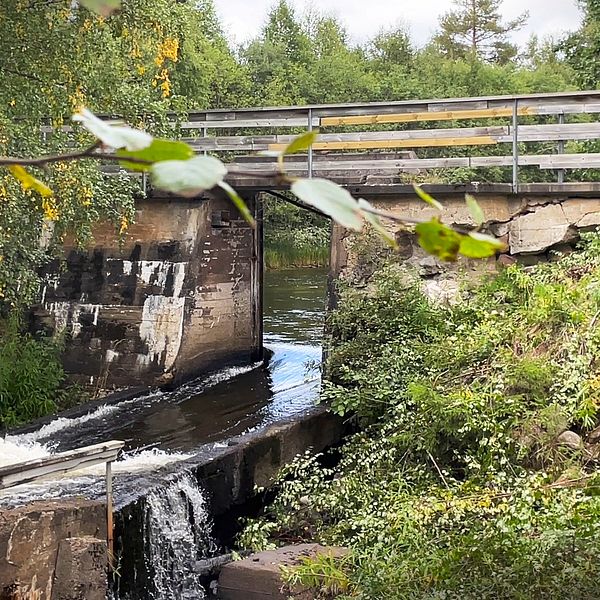 En bild på en sliten kraftverksdam, man kan skymta en slags bro som går över ett vattendrag.