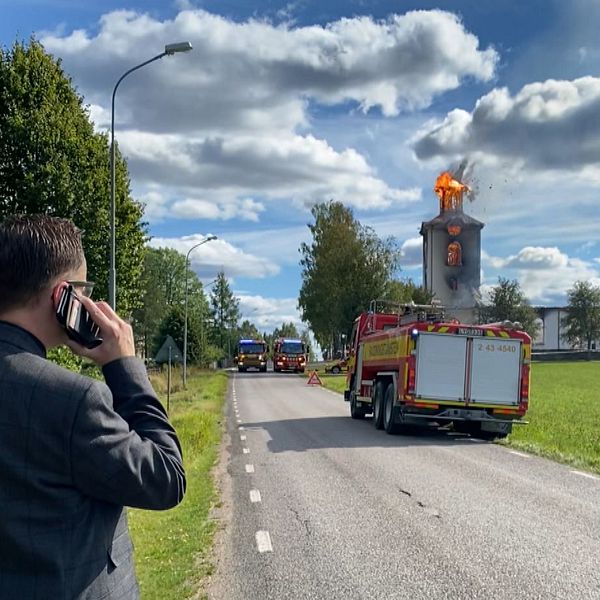 Man med mobiltelefon mot örat tittar mot en brandbil och en brinnande kyrka.