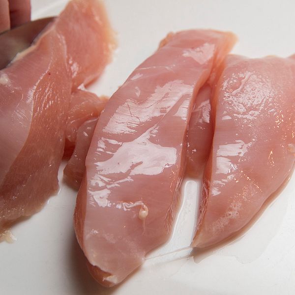 Råa kycklingfiléer blir skurna i bitar av en hand med kniv.