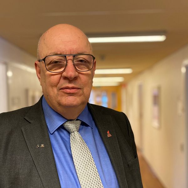 En man (politiker vid namn Ulf berg (M)) har glasögon och kostym och tittar in i kameran – bakom en korridor