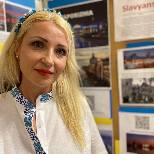 Viktoriya Lunova står framför en vägg med bilder från Ukraina.