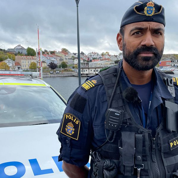 Medelålders man med mörkt, ganska kort skägg, ståendes framför en polisbil i Strömstads hamn. Han bär kortärmad mörkblå polisuniform och en polismössa.