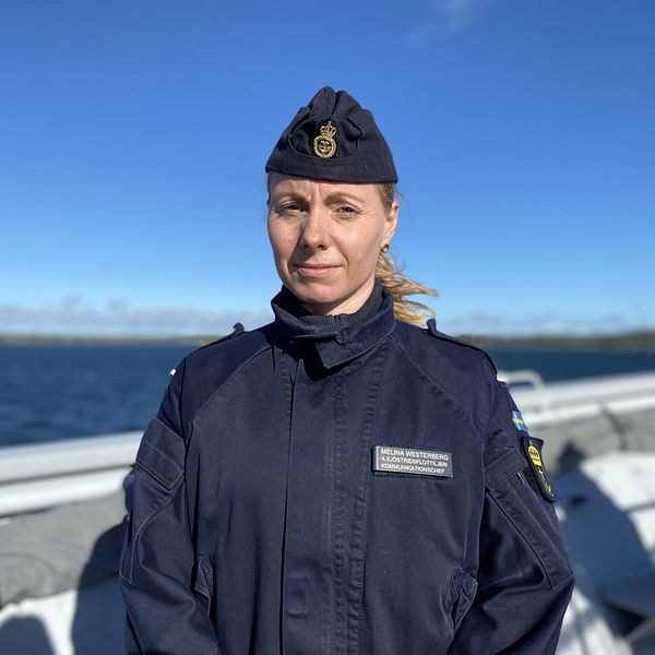 Melina Westerberg från försvarsmakten står på en båt i skärgården med blå bakgrund. Hon har uniform och kisar mot solen.