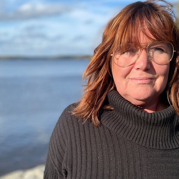 Bild på Eskilstunas stadsbyggnadsnämnds ordförande, Sarita Hotti (S). Hon har rött hår med pannlugg. Hon har på sig en svart polotröja och pilotglasögon. I bakgrunden skymtar Mälarem och grön växtlighet.