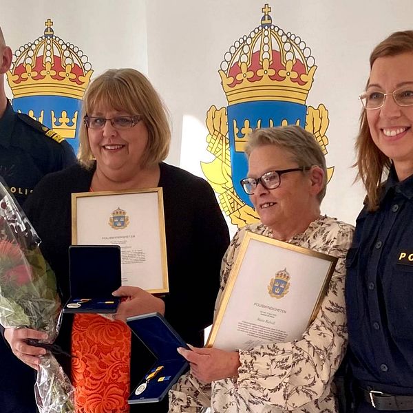 Två poliser och Anneli Gustafsson och Marie Ridvall ler med diplom och blomsterbuketter i samband med utdelningen av medborgarmedaljer för insatsen vid branden i en radhuslänga i Bergvik.