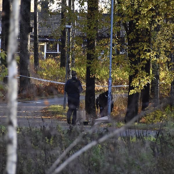 två personer ses på håll vid cykelbana i skogsområde, hus i bakgrunden