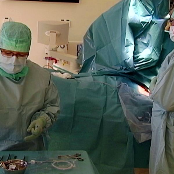 Genrebild på pågående operation i kirurgisal där sjukvårdspersonal arbetar iklädda skyddskläder och munskydd.
