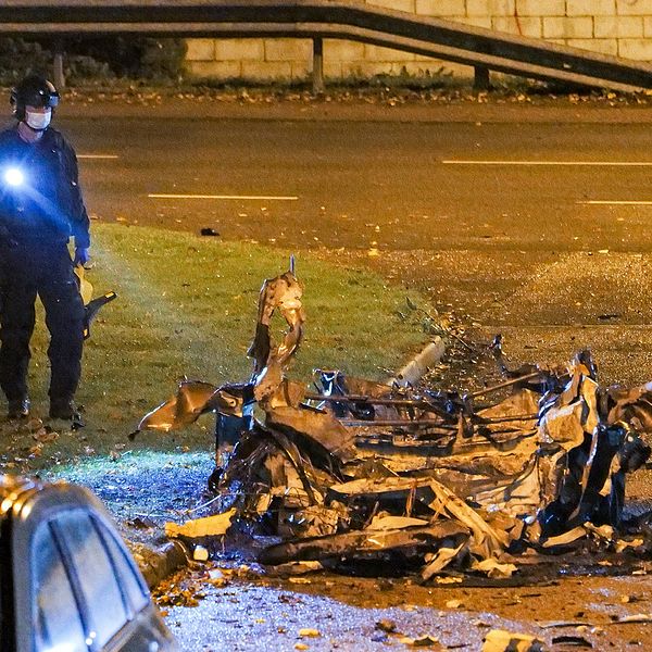 En polis står och lyser med en ficklampa på en ett förvridet skrotskelett från en bil.