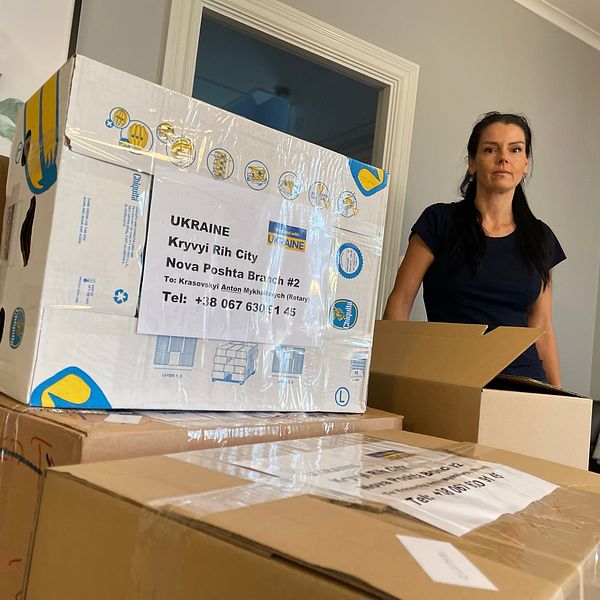 Bild på en svartklädd kvinna bredvid en låda där det står Ukraina. Lådan är från den ideella föreningen Ukrainas vänner som hjälper ukrainare i Uddevalla. Kvinnan på bilden heter Anneli Lillmaa och var med och startade föreningen.