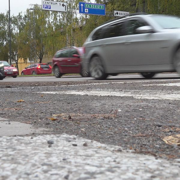 En asfalterad väg med mycket trafik, några av bilarna swishar suddigt förbi. I bakgrunden syns vägskyltar mot centrum, E4 södra och Backen.