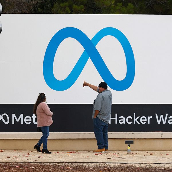 Bilden föreställer två människor som står framför Metas skylt vid huvudkontoret i Kalifornien.