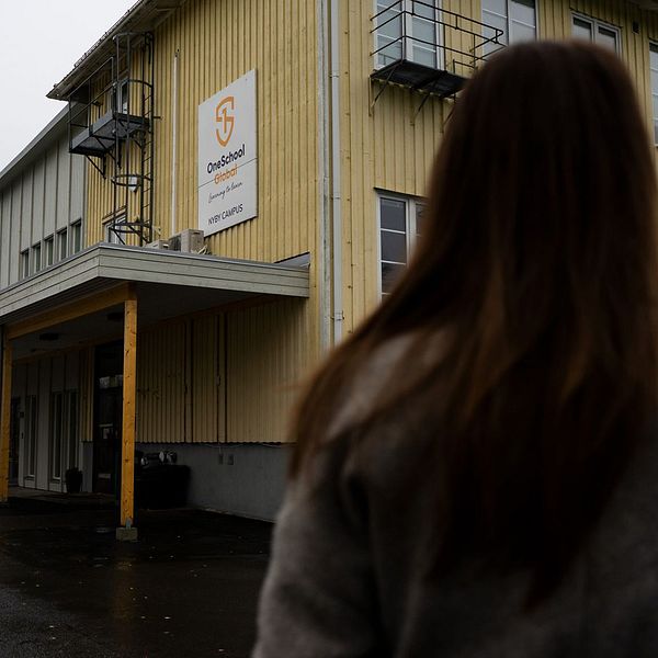 En bild bakifrån på en person med långt hår som står framför Oneschool globals gula skolbyggnad.