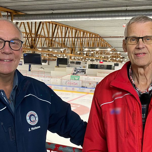 Två män står inne i en ishockeyarena. Båda har glasögon och kort grått hår. Mannen till vänster, Janne Mattson, har blå jacka och mannen till höger, Göran Håkansson, röd jacka. Båda har klubbemblem från Mörrum Hockey på kläderna.