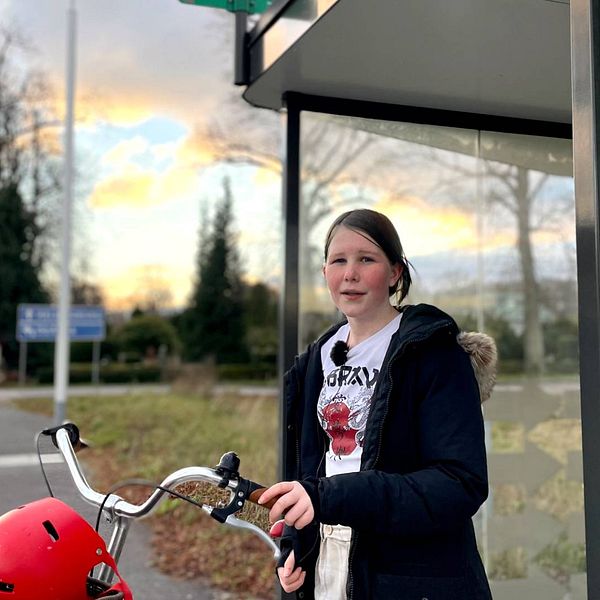 Flicka står vid sin cykel vid en busskur i Allerum