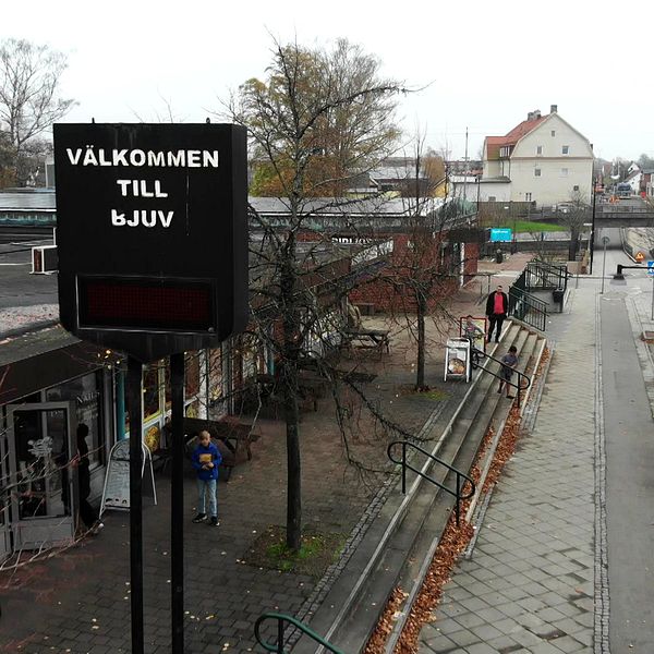 Välkomstskylt till Bjuv, gågata med höstlöv och byggnader i bakgrunden.