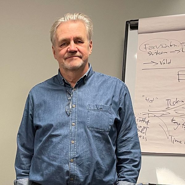 Psykologen Magnus von Campenhausen på Manscentrum står iklädd en blå skjorta framför en whiteboardtavla med förklaringar om hur våldsamhet fungerar.