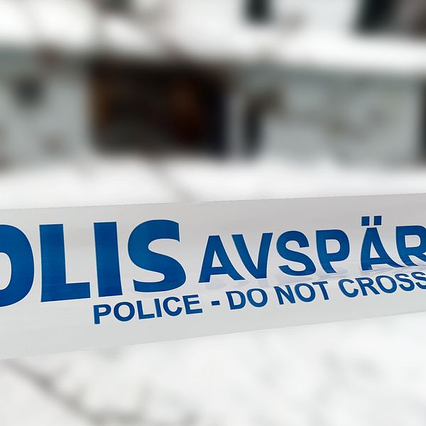 Bild på polisens blå-vita avspärrningsband i förgrunden. Bakgrunden är väldigt blurrad eftersom det visar ett bostadshus intill.