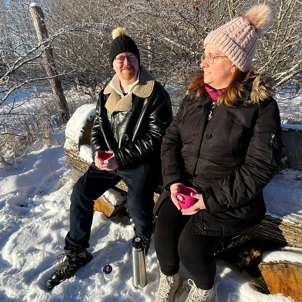 Två kvinnor sitter på en bänk i ett vinterlandskap med snö och sol.