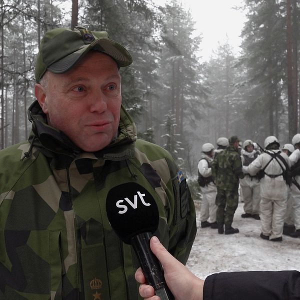 Reporter intervjuar soldat i vinterkamouflage i skogsmiljö, fler soldater i bakgrunden.