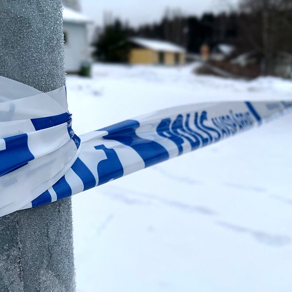 Bild på polisens avspärrningsband som sitter runt en lyckstolpe och ett träd på andra sidan. Marken är snötäckt.