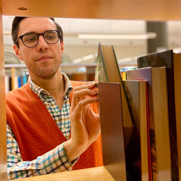 Bibliotikarie Erik Hägg plockar fram en bok i en av bokhyllorna på Hudiksvalls bibliotek och förklarar hur bibliotekens självservice fungerar.