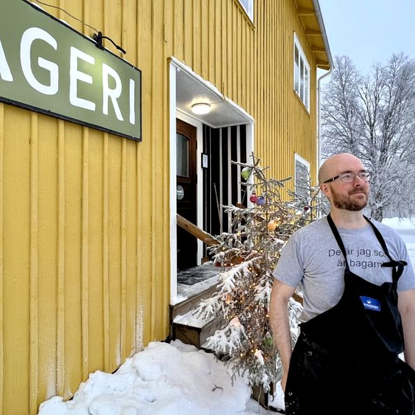 Bagaren Martin Jonsson står utanför bageriet i Granö, en gul villa. Det är vinter och snö på vägen. Bakom honom står en snöig julgran.