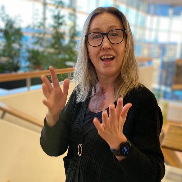 Anna Sofia Såthe – en medelålders kvinna med glasögon – gör teckenspråkets tecken för leva.