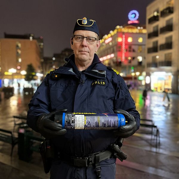 Polis Anders Lindberg står i polisuniform på Medborgarplatsen i Stockholm. Han håller fram en lustgastub mot kameran.