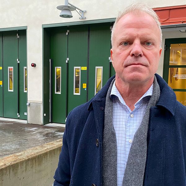 Fredrik Forselius, som är ambulanschef vid Region Dalarna och bär en blå rock, står framför ett ambulansgarage med gröna portar och berättar om det svåra personalläget.