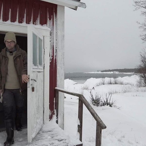 Noak Larsson kommer ut från ett snöigt rött hus med vita knutar i Bjuröklubb. Det är vinter och mycket snö på marken. I bakgrunden kan man se Bottenviken.