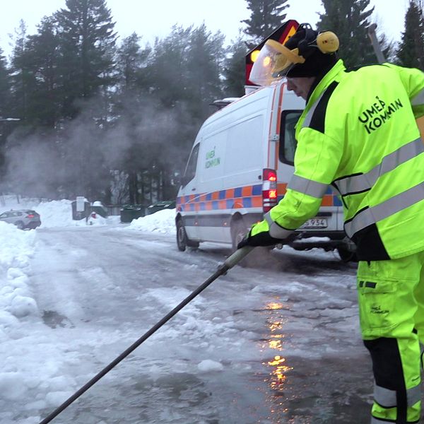 Man med varselkläder som står med ett verktyg som används för att tina upp brunnar. Det är vinter och snö. Bakom honom står en skåpbil från Umeå kommun.