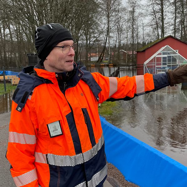En man i skyddskläder pekar ut mot ett översvämmat område.
