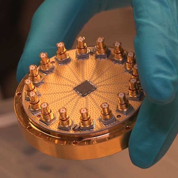 En del av en kvantdator hålls upp av en person i gummihandskar.