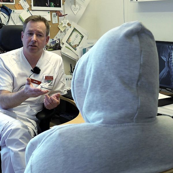Läkare diskuterar med patient i huva framför en datorskärm som visar röntgenbilder.